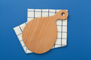 Cutting board with napkin on color background, top view