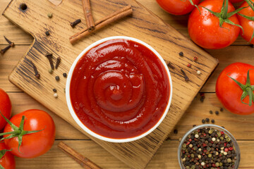 Delicious ketchup with spices and tomatoes on wooden background, top view