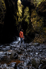 Obraz premium Adventurer exploring a narrow, moss-covered canyon with a flowing stream and dramatic cliffs