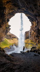 A man standing behind the Kvernufoss waterfall in Iceland, surrounded by lush green moss and rugged rocks