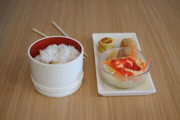 Japanese food in white box with chopsticks on wooden table background.
