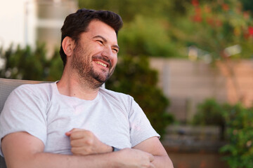 Lonely cheerful positively smiling bearded middle-aged man sits outdoors at sunset. Happy life concept