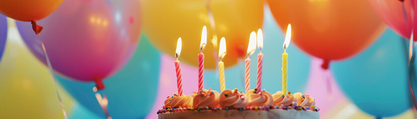 Frosted birthday cake with lit candles and colorful balloons, creating a festive and happy celebration