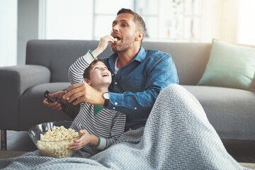 Dad, tv remote and kid with popcorn by sofa for entertainment, snack and watching cartoon together. Family, father and son with feeding at home for care, love and streaming of show in living room