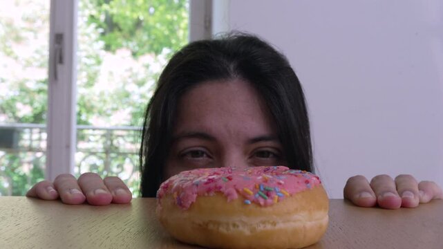 A woman peeking over a table, eyes focused on a colorful sprinkled donut, embodying the theme of delayed gratification and temptation, with a playful and curious expression