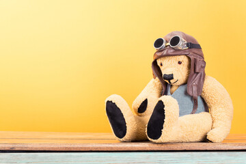 Vintage Teddy Bear toy in leather aviator's hat and goggles front yellow wall background. Retro old...