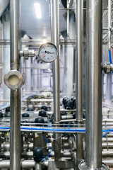 Large industrial stainless steel pipes and pressure gauge in modern brewery