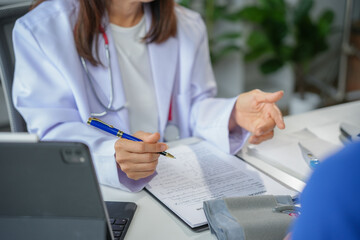 Female doctor listens and writes medical notes during a consultation in a hospital, showing empathy...