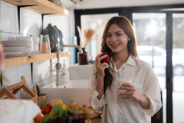 Young woman happily eating a healthy breakfast in her cozy kitchen, featuring fresh fruit and milk