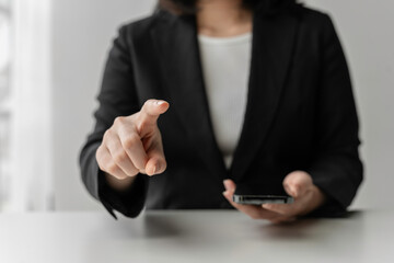 Businesswoman is pointing her finger to the left while holding a smartphone in her other hand, suggesting a dual focus on technology and direct communication