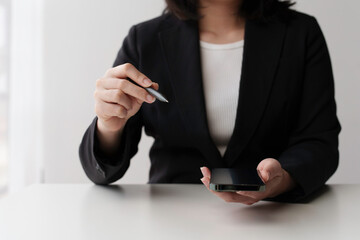 Confident businesswoman in stylish suit holding smartphone and pen during online meeting in modern office setting, showcasing leadership skills and professionalism