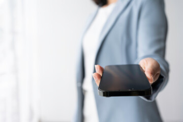 Confident businesswoman showcasing smartphone with blank screen in professional setting, ready to present important information. Modern device connects to digital world, perfect for app display