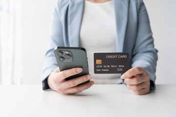 Businesswoman is holding a credit card and using a smartphone, likely making an online purchase or managing her finances