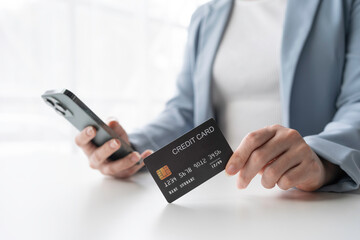 Businesswoman is holding a credit card and using her smartphone, likely making an online purchase or managing her finances