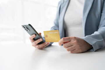 Businesswoman is making an online payment using a credit card and a smartphone. She is sitting at a desk in her office