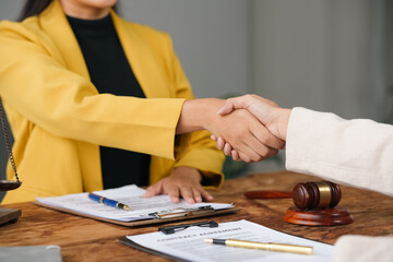 Two female lawyers shaking hands after signing a contract agreement in an office, with legal...
