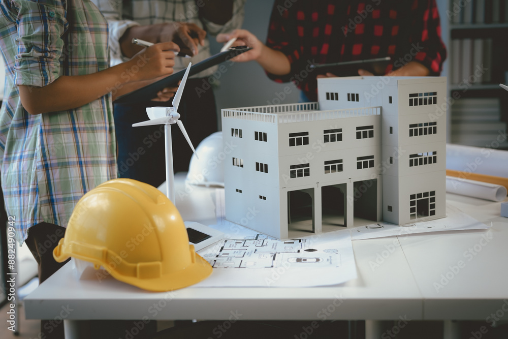 Wall mural architects team working on a project of a sustainable building with a wind turbine, discussing about