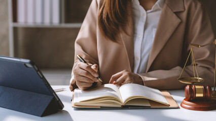 Focused female lawyer takes notes in her office, surrounded by legal documents and symbols of...