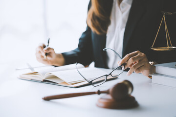 Lawyer is taking off her eyeglasses while writing in a notebook at her desk, with a gavel and...