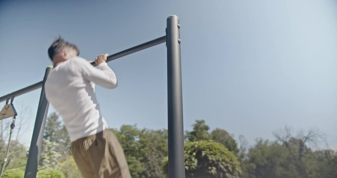 A man exercises on parallel bars in the park, performing pull-ups under clear blue skies on a sunny day, demonstrating strength and dedication to fitness.