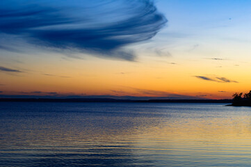 Fototapeta premium As dusk falls over the St. Lawrence River near Montreal, the horizon is alight with vibrant hues of orange and blue, while swirling clouds above mirror their vivid dance on the serene river's surface