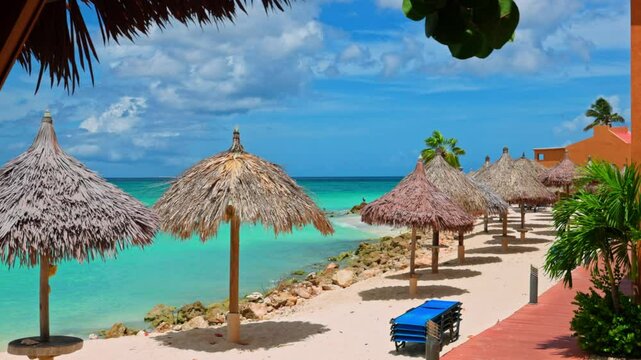 View featuring pathway two-story hotel buildings along Caribbean Sea coastline with beach with thatched umbrellas and lounge chairs.
