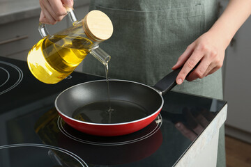 Vegetable fats. Woman pouring oil into frying pan on cooktop in kitchen, closeup