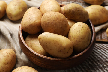 Many fresh potatoes in bowl on wooden rustic table, closeup