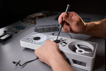 A technician is skillfully repairing a computer GPU fan with precision tools in a workshop