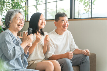 家のリビングでソファでテレビを見ながら盛り上がる祖父母と孫の女の子
