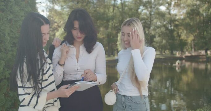 A female group of university students enjoy a break in a lush park, engaging in a friendly chat about their studies.
