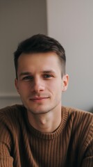 Fototapeta premium Cheerful young man in his 20s with brown hair and blue eyes smiles happily in a portrait indoors, exuding confidence and positivity against a neutral background