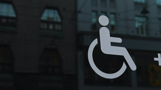 A symbol of wheelchair accessibility displayed on a window in an urban environment