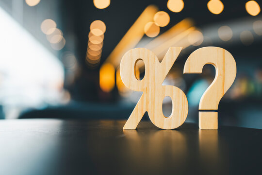 Percentage and question mark on wood table in blur urban background, raising or lowering Fed interest rates to correct inflation concepts.
