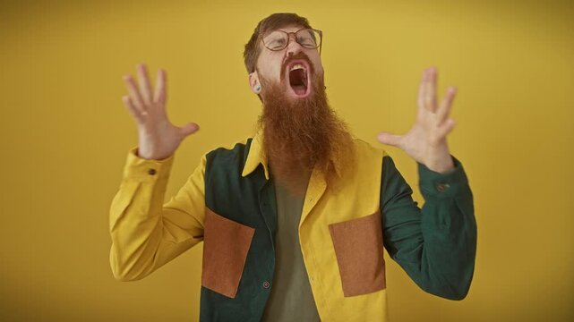 Frustrated redhead man in glasses kicks off a crazy rant, arms flailing madly over isolated yellow backdrop