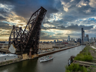 River boat passes under the St. Charles Air Line Bridge, steel railroad drawbridge over the Chicago river with dramatic sunset sky