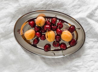 Fresh ripe apricots and cherries on a metal oval plate on a light background