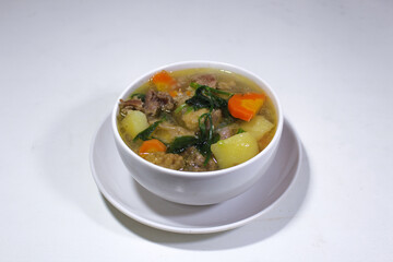 boiled meat vegetable soup served in a porcelain bowl and served on a white plate with a plain white backgorund