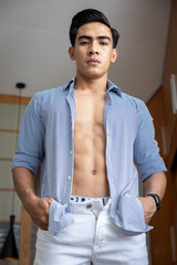 Handsome and good looking single gym fit and muscled male model with a black fashionable hairstyle and dark eyes, wearing a blue formal shirt that is open, revealing his abs and sixpack