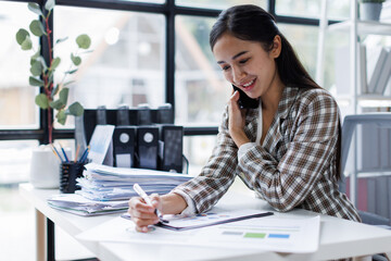 Asian Business woman using calculator and laptop for doing math finance call phone on an office desk, tax, report, accounting, statistics, and analytical research concept