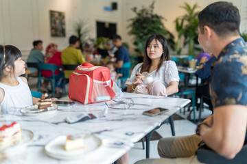 A family of five, consisting of Chinese and Indian Malaysian adults, children, and a baby, enjoying a gathering at a stylish cafe in Selangor, Malaysia, on an early summer afternoon.