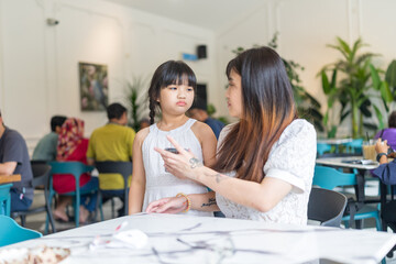 A twenty-something Malaysian woman and a six-year-old girl spending time together at a stylish cafe in Selangor, Malaysia, on a sunny early summer afternoon.