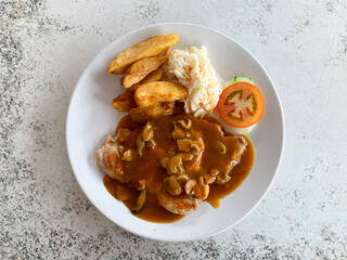 grilled golden bbq chicken chop pork cutlet meat with French fries wedges, coleslaw salad tomato and mushroom brown cream sauce in white plate on marble table western cafe halal food restaurant menu