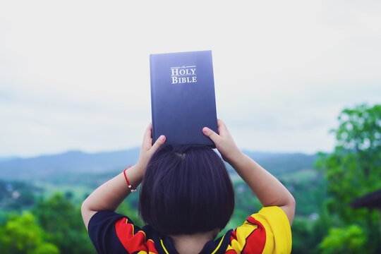 little girl happy with Bible in morning on mountain with copy space, christian concept.