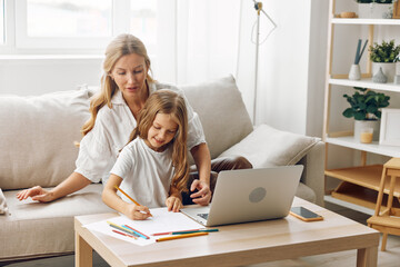 Mother and daughter bonding on cozy couch while exploring educational content on laptop in bright living room