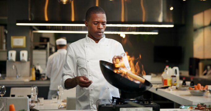 Black man, chef and fire with frying pan in kitchen at restaurant for fine dining, meal and creativity. Employee, professional and cook with food for culinary, hospitality and catering service