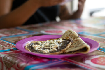 Photograph of delicious and authentic regional Mexican food consisting of: tortilla, beans and cheese, at a local street food stall and served on a table with a traditional tablecloth