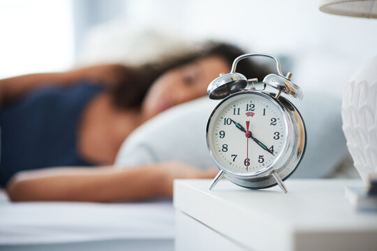 Alarm, clock and woman sleeping in bed with depression, tired or anemia and low energy or fatigue at home. Time, late and person dreaming, relax or lying with risk of iron deficiency or hypersomnia