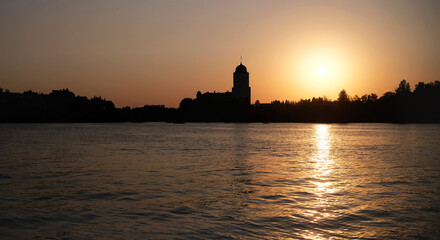 The medieval Vyborg castle with tower on sunset. Waterfront view of silhouettes