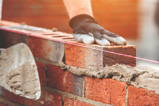Close Up Of Bricklayer's Hand Placing  Brick On Wall